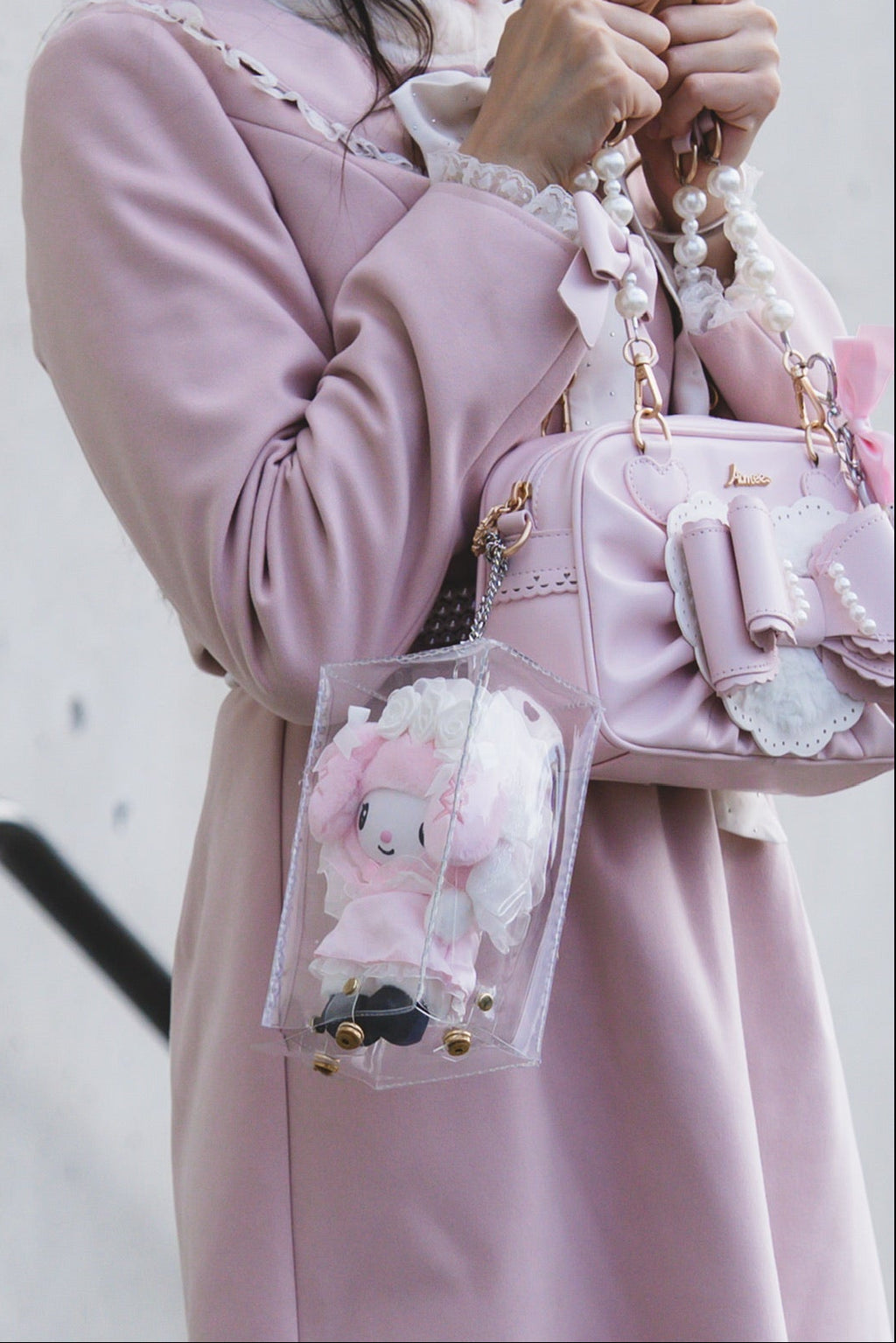 Person wearing a pink coat holding a matching pink handbag with floral design against a plain background